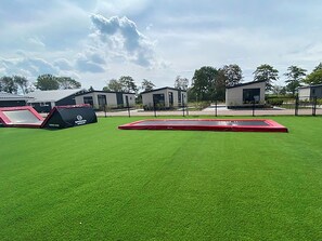 An outdoor area with artificial grass, a red trampoline, and a black and red play structure. - Wonderful private villa for 2 people with A/C, pool, WIFI, TV and terrace (Tholen)