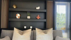 A modern living room with a grey sofa, three decorative pillows, and a black shelving unit with various items. - Wonderful private villa for 2 guests with pool, WIFI, A/C, TV and terrace (Tholen)