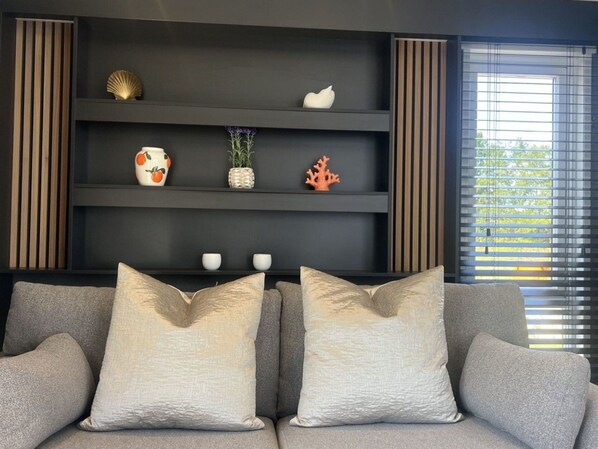 A modern living room with a grey sofa, three decorative pillows, and a black shelving unit with various items. - Wonderful private villa for 2 people with A/C, pool, WIFI, TV and terrace (Tholen)