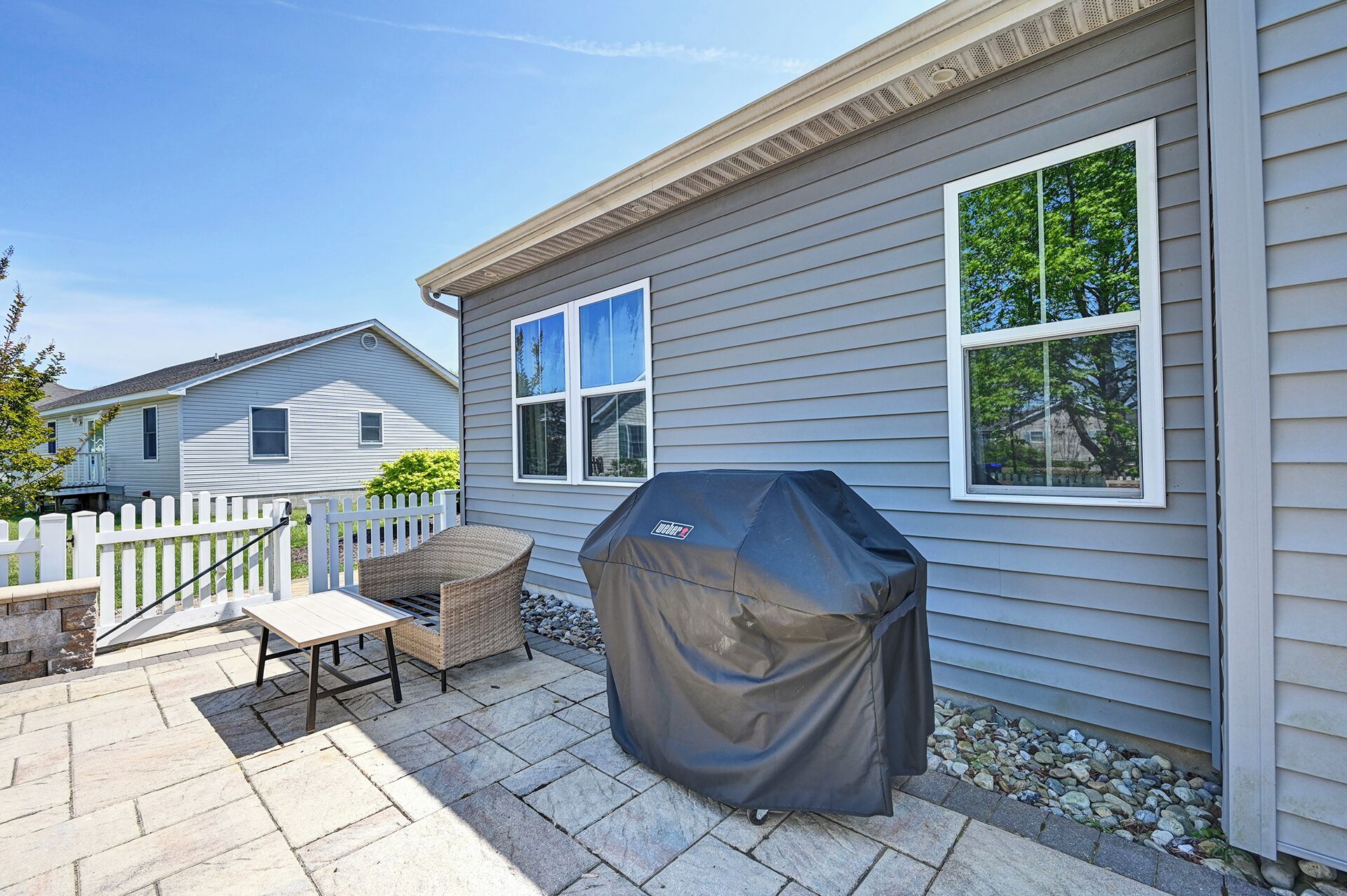 Une terrasse avec un barbecue, une chaise en osier et une table.