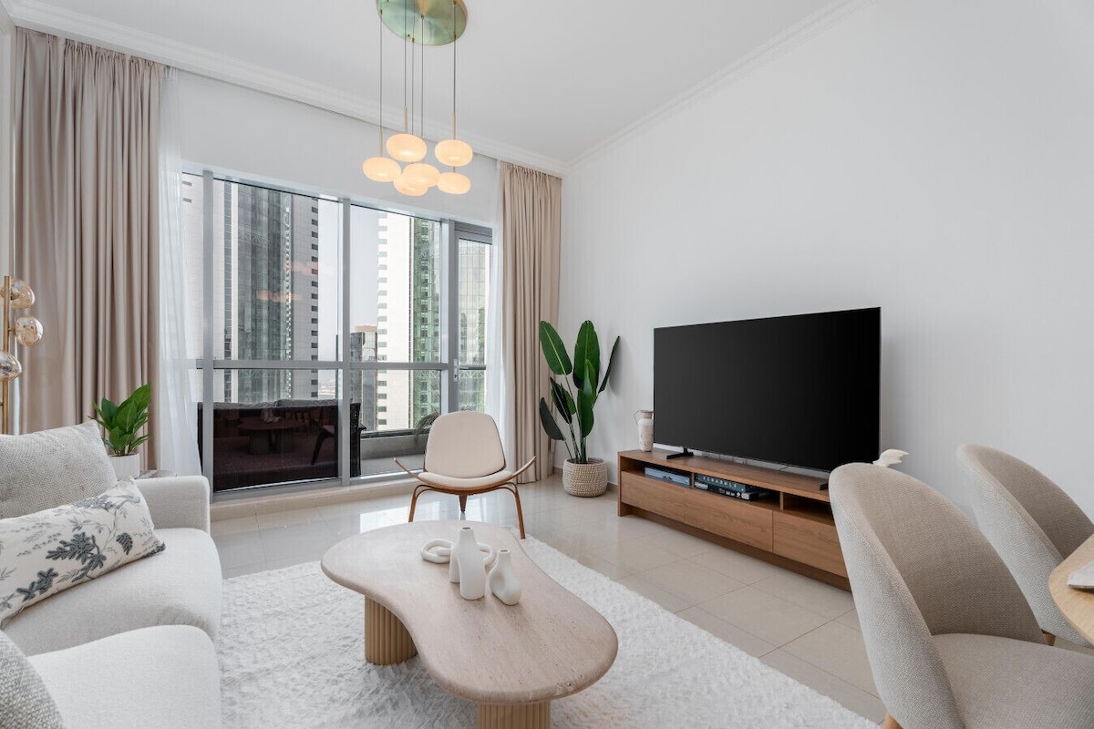 Ein modernes Wohnzimmer mit großem Fernseher, bequemen Sitzmöglichkeiten, einem Couchtisch und einem Balkon mit Blick auf die Stadt.