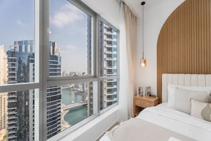 Ein modernes Hotelzimmer mit großem Fenster und Blick auf die Stadt, einem Bett mit weißer Bettwäsche und einem Holzkopfteil.