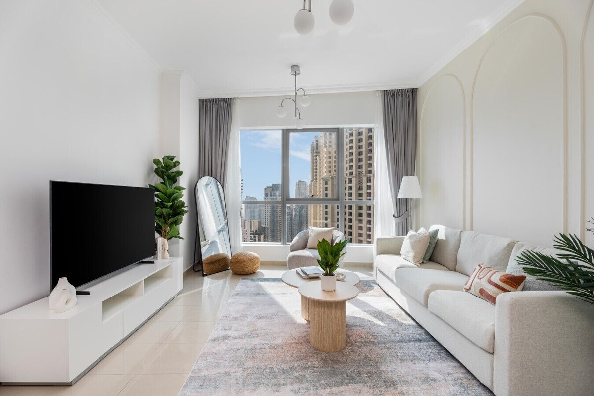 Ein modernes Wohnzimmer mit Flachbildfernseher, einer Couch, einem Couchtisch und einem großen Fenster mit Blick auf die Stadt.