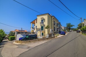 Eine Wohnstraße mit einem zweigeschossigen Gebäude, parkenden Autos und blauem Himmel.