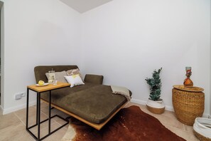 Ein Schlafzimmer mit einem Bett, einem kleinen Tisch, einer Topfpflanze und einem Weidenbeistelltisch.