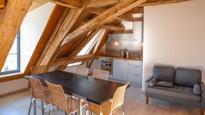 A modern loft with exposed wooden beams, a dining area with wicker chairs, a kitchenette, and a gray sofa. - Apartment 'Ferienwohnung Wintersulgen' with Wi-Fi (Heiligenberg)