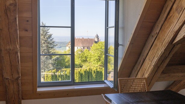 A room with a large window, wooden beams, a table, and a chair. - Apartment 'Ferienwohnung Wintersulgen' with Wi-Fi (Heiligenberg)