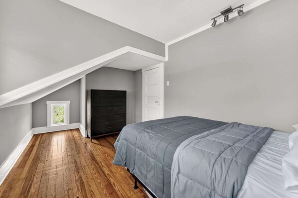 A bedroom with a sloped ceiling, a bed, a window, and a door.