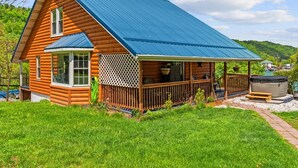 Eine Holzhütte mit blauem Dach, einer Veranda und einem Whirlpool im Garten.