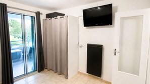 Une pièce dotée d’une porte-fenêtre coulissante, d’un téléviseur à écran plat fixé au mur et d’un petit appareil électroménager noir.