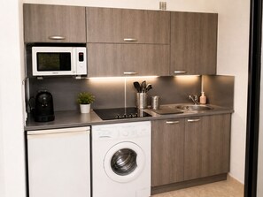 Une cuisine compacte équipée d’un four à micro-ondes, d’une machine à café, d’un évier et d’un lave-linge.