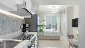 A modern kitchen with a gas stove, a built-in oven, and a stainless steel sink. There is a dining area with a table and chairs, and a large window offering a view of the city. - Gala Guests - Lakeside Tower Living (Dubai)