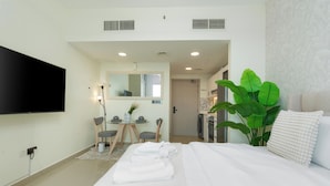 A hotel room with a bed, a TV, a desk with chairs, and a large plant. - Gala Guests - Lakeside Tower Living (Dubai)