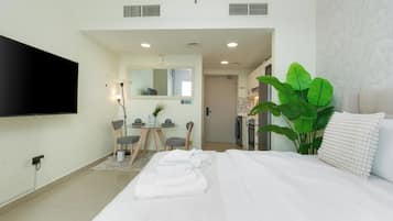 Quarto de hotel com cama, televisão, secretária com cadeiras e uma planta grande.