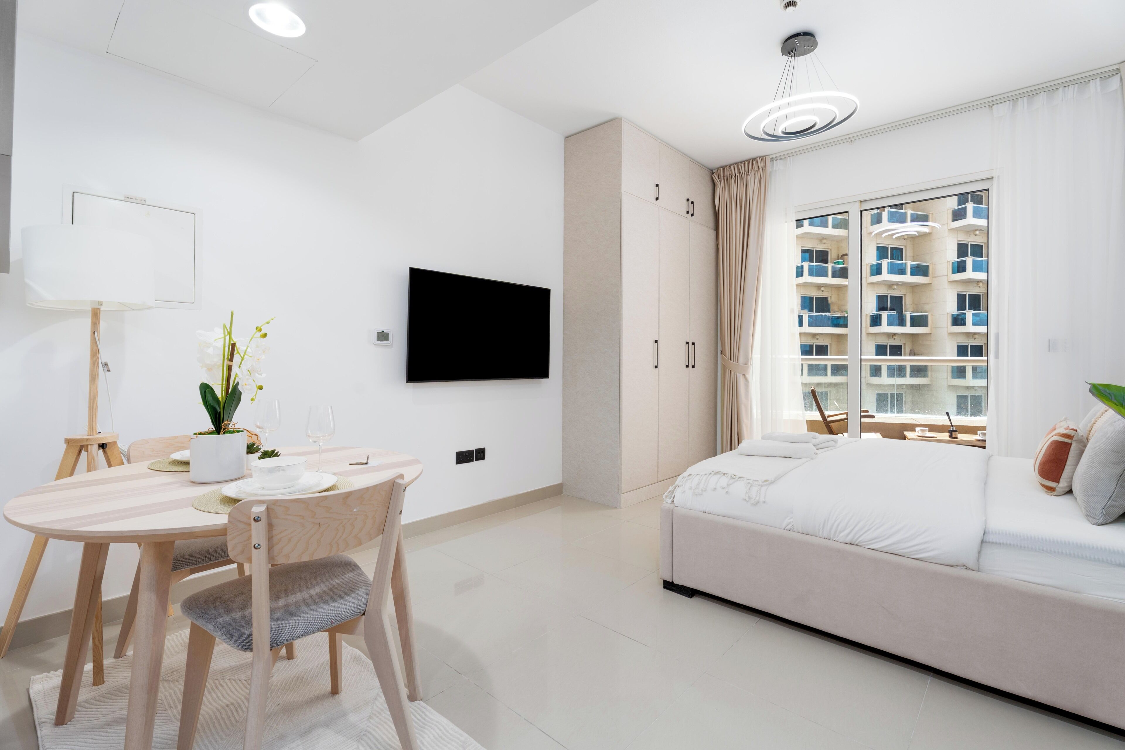 Ein modernes Hotelzimmer mit Essbereich, einem Flachbildfernseher, einer Couch und einem großen Fenster mit Blick auf das Gebäude.