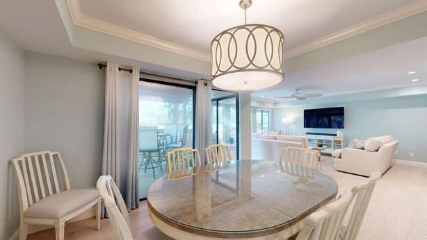 A modern dining area with a glass table, white chairs, and a central light fixture. - Significant Golf Views from this 3-Bedroom Fazio Villa (Hilton Head)