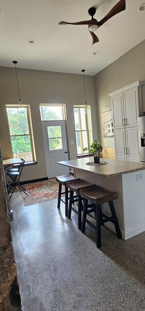 A kitchen with a central island, bar stools, a ceiling fan, and large windows.