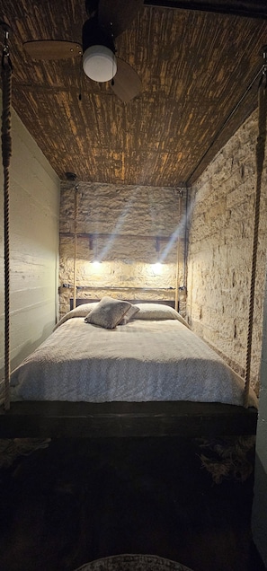 A room with a bed, a ceiling fan, and a light source.