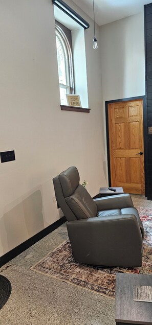 A modern living room with a leather sofa, a small table, a rug, a wooden door, and a mirror on the wall.