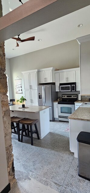A kitchen with white cabinets, a refrigerator, an oven, a microwave, and a ceiling fan.