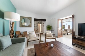 Ein Wohnzimmer mit Sofa, Sesseln, Couchtisch, Fernseher und einem großen Spiegel.