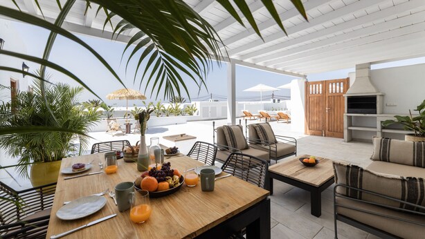 An outdoor dining area with a wooden table, chairs, and a view of the ocean. - Villa Roseta by Escape Home (Puerto del Carmen)
