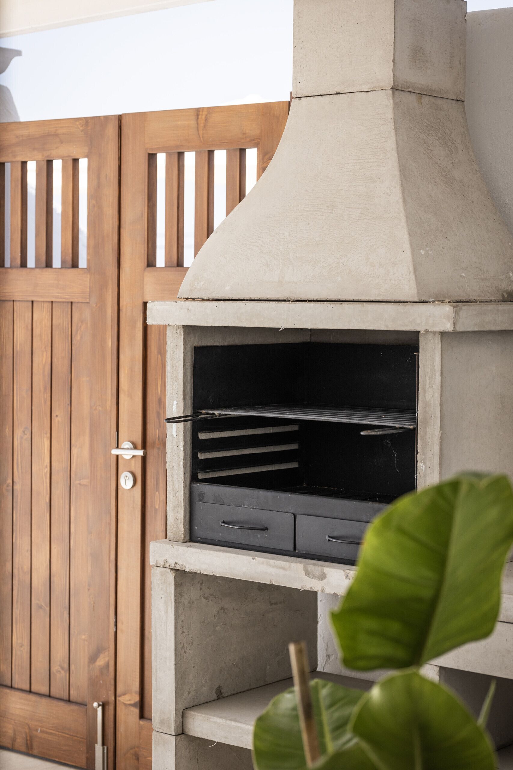 Um forno de concreto ao ar livre com porta de madeira e puxador de metal, cercado por uma vedação de madeira.