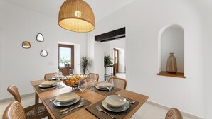 A dining room with a wooden table set for four, surrounded by wicker chairs, a hanging light fixture, and a plant in the background. - Villa Roseta by Escape Home (Puerto del Carmen)