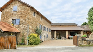 A stone building with a covered driveway, a wooden fence, and a green sign. - Gîte "La Grange d'Émile" with Private Garden and Wi-Fi (Chozeau)