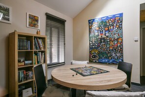 Une pièce avec une table ronde, une bibliothèque et un grand tableau coloré accroché au mur.