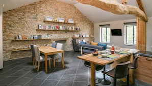 A spacious loft with a stone wall, wooden beams, a dining area, and a seating area with a sofa and chairs. - Gîte "La Grange d'Émile" with Private Garden and Wi-Fi (Chozeau)