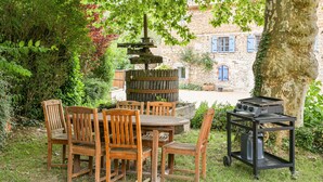 An outdoor dining area with a wooden table and chairs, a grill, and a stone wall in the background. - Gîte "La Grange d'Émile" with Private Garden and Wi-Fi (Chozeau)