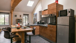 A modern kitchen with wooden cabinets, a stainless steel refrigerator, and a microwave. There is a dining area with a table and chairs. - Gîte "La Grange d'Émile" with Private Garden and Wi-Fi (Chozeau)