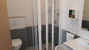 A bathroom with a glass-enclosed shower, a toilet, and a sink.