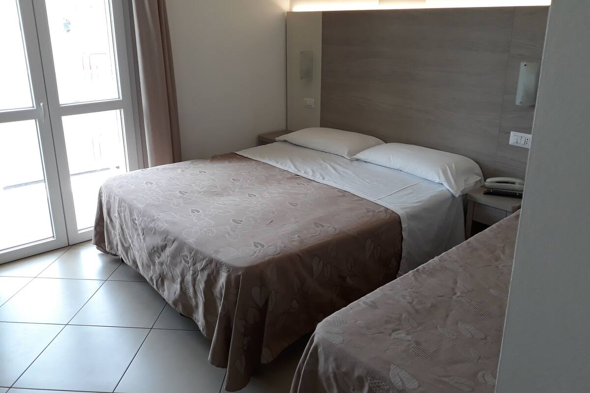 Quarto de hotel com cama, mesa de cabeceira e janela com cortinas.