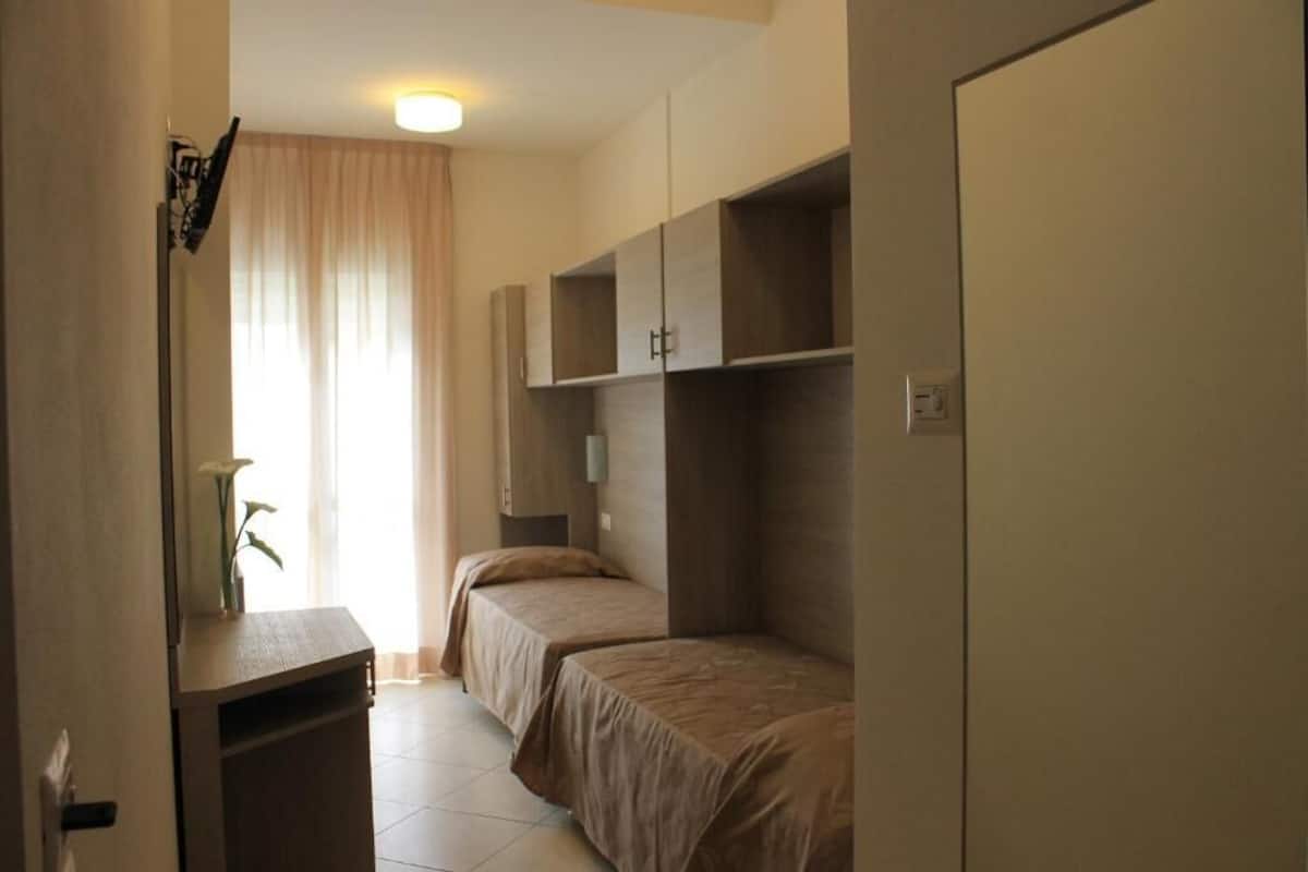 Quarto com duas camas, uma escrivaninha e um guarda-roupa.