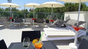 Terraza en la azotea con sillones, sombrillas y una mesa con bebidas.