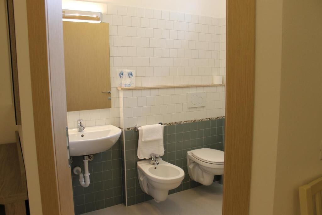 Un bagno con lavandino, bidet e WC, pareti piastrellate e uno specchio.