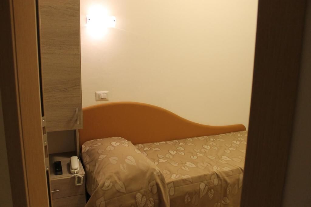 A single bed with a headboard, a bedside table with a lamp, and a wall-mounted light fixture.