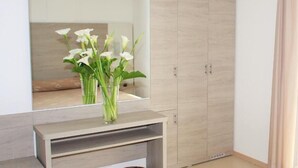 Una habitación con televisor montado en la pared, un espejo que refleja un florero de flores blancas, un armario y una consola.