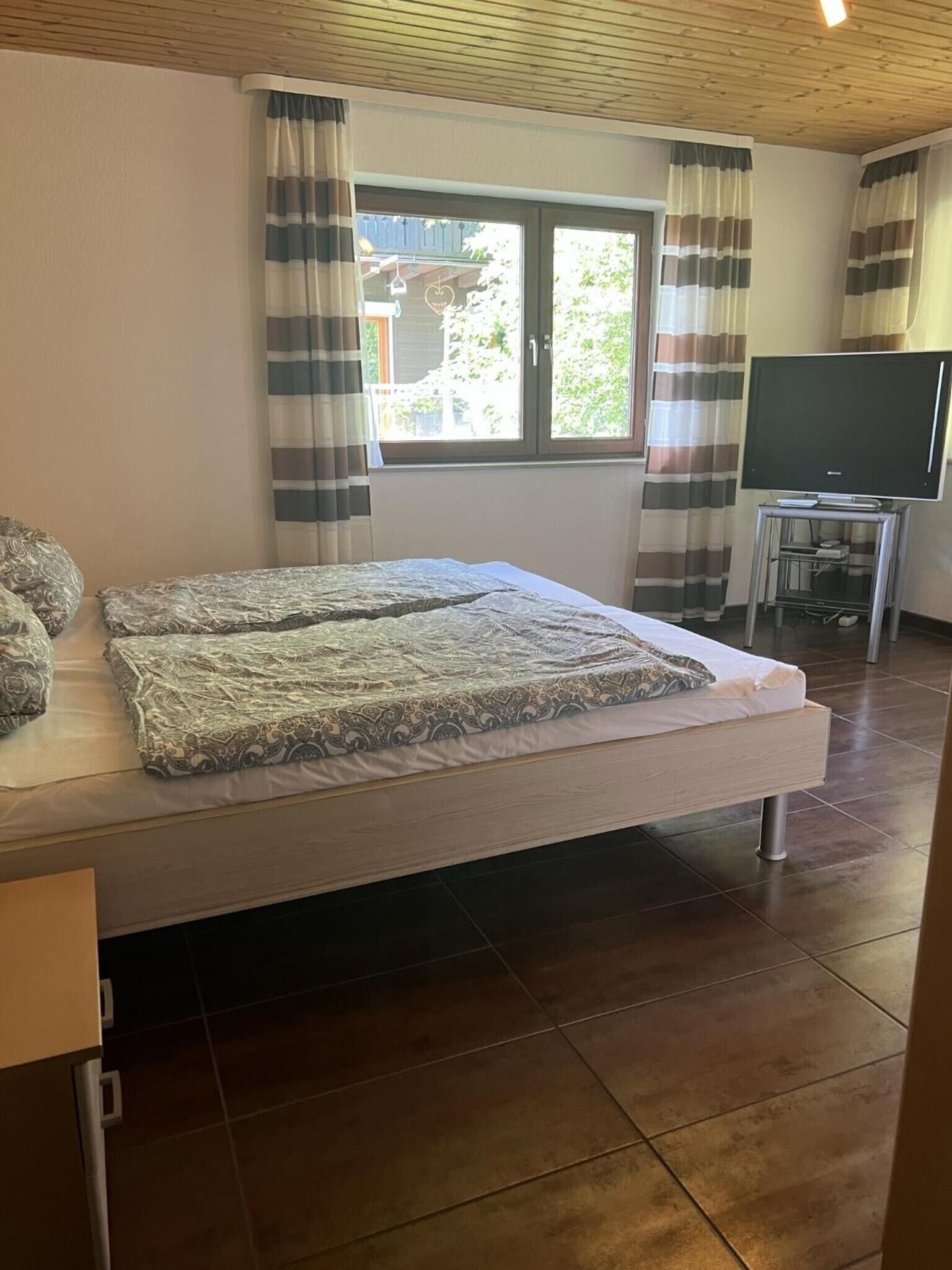 Une chambre à coucher avec un lit, des rideaux, une télévision et une fenêtre.
