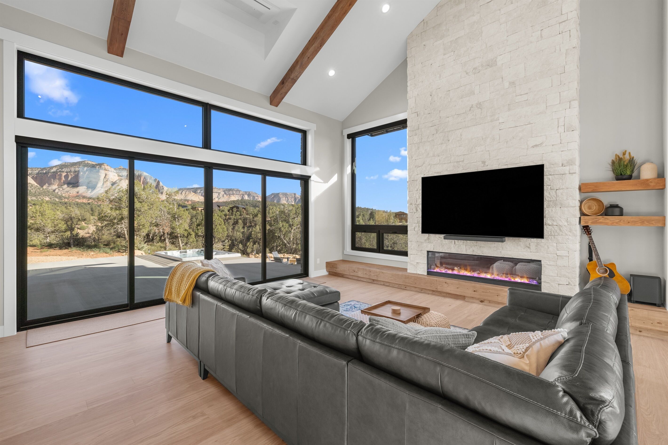 A modern living room with a large gray sectional sofa, a flat-screen TV mounted on a white brick wall, and a fireplace.