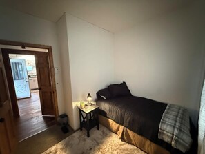 Ett sovrum med en säng, ett litet bord med en lampa, en dörr som leder ut till en balkong och en vit vägg.