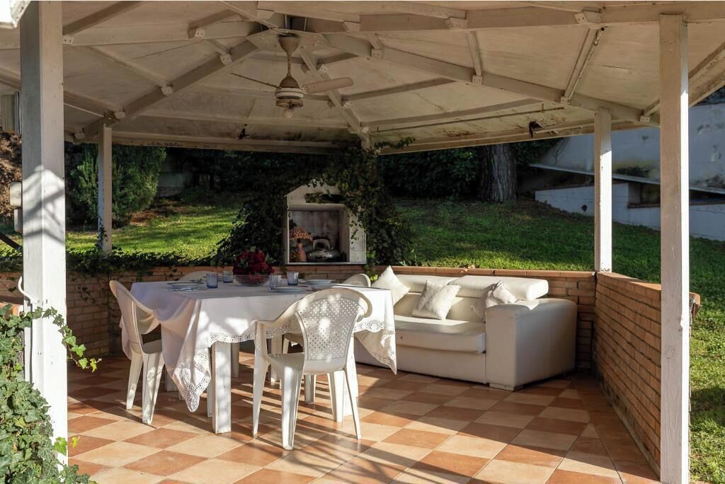 Un patio exterior con mesa, sillas y sofá bajo una pérgola.
