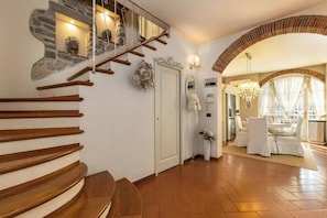 A staircase with wooden steps, a stone wall, and a dining area with white furniture. - [TUSCANY]Villa with Pool, Jacuzzi and Gym (Serravalle Pistoiese)