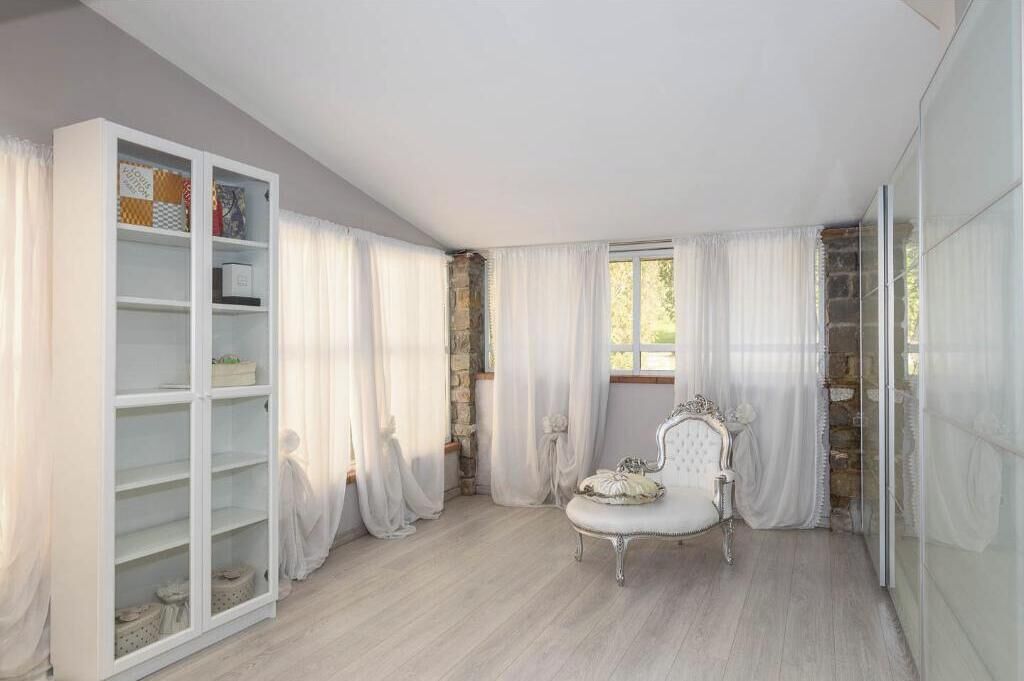A room with a white wardrobe, a white chair, and a window with curtains.