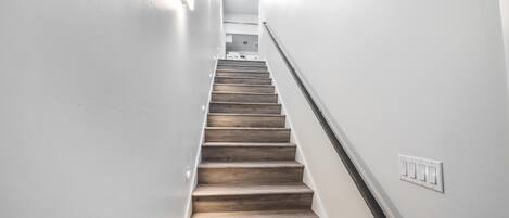 Una scala con gradini in legno, pareti bianche e un interruttore a muro.