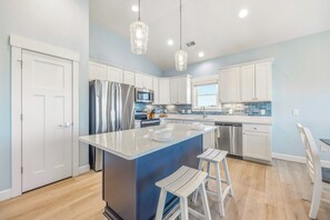 Eine moderne Küche mit Kochinsel, weißen Schränken, Edelstahlgeräten und Pendelleuchten.