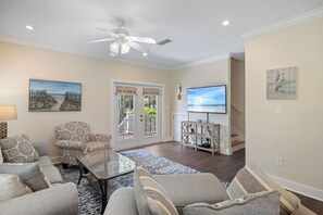 A living room with a ceiling fan, a television, and a view of the outdoors through a glass door. - Vacation Home Near Beach by PKRM (Pensacola)