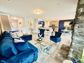 Een moderne woonkamer met een blauwe zithoek, een salontafel en een eetgedeelte met een blauwe stoel.